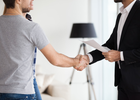 young couple, family at meeting making deal, signing contract with realtor, landlord, banker. husband handshaking with man in suit. concept of meeting with client, customer. close up handshake.