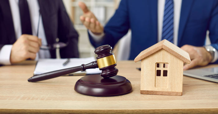 gavel and wooden house on a table in a legal office with two lawyers discussing property matters