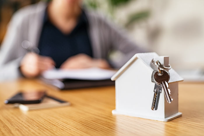 model house with keys on table nearby person writing notes important for home ownership